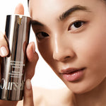 Woman holding a skincare product labeled ' Ourself ADVANCED REGENERATIVE SERUM' against a neutral background