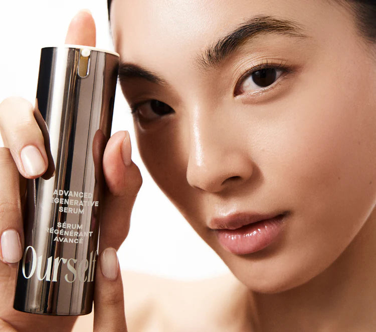 Woman holding a skincare product labeled ' Ourself ADVANCED REGENERATIVE SERUM' against a neutral background