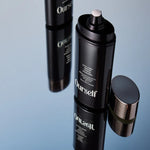 Black cosmetic bottles with 'Ourself Intelligent Defense Mineral Sunscreen Broad Spectrum SPF 50' branding on a reflective surface.