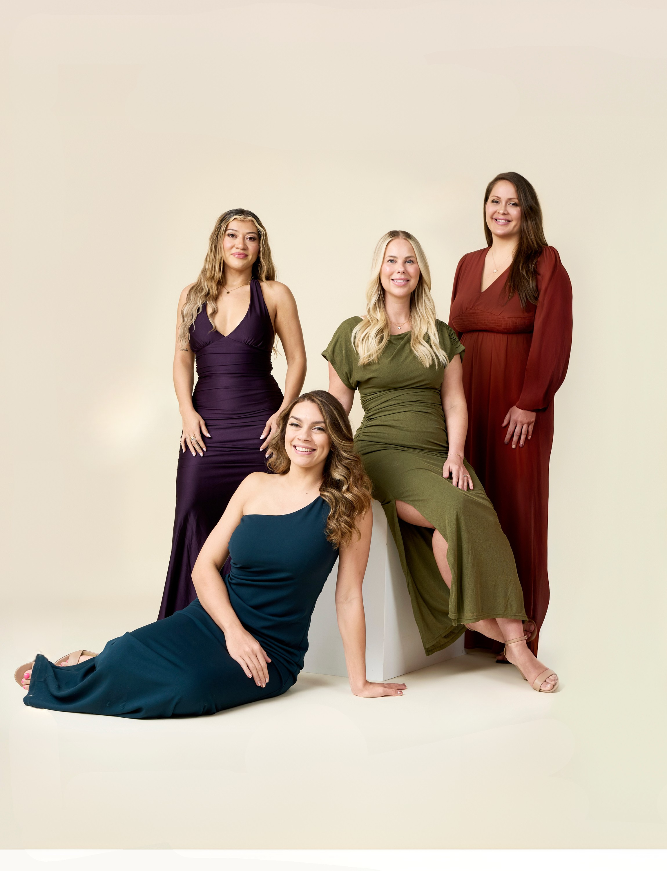 Group of women in colorful dresses posing against a beige background