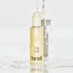 Skincare bottle labeled 'Ourself' on a marble surface with water droplets.