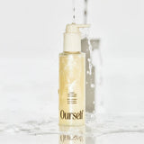 Skincare bottle labeled 'Ourself' on a marble surface with water droplets.