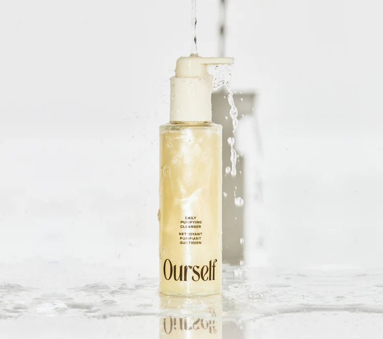 Skincare bottle labeled 'Ourself' on a marble surface with water droplets.